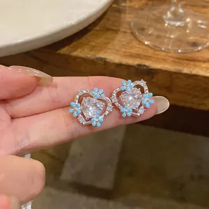 Close-up of heart-shaped stud earrings with blue enamel flowers and sparkling crystals