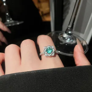 Elegant close-up of a sparkling flower zircon ring featuring a vibrant green center stone on finger