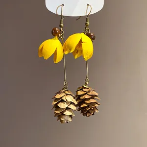 Detailed view of vintage forest style drop earrings with yellow flowers and pinecones.