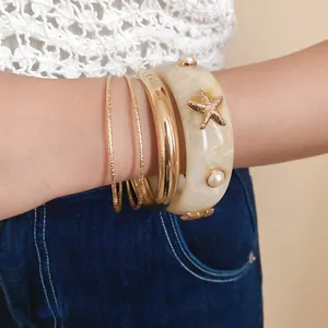 Bohemian style resin starfish bracelet and gold bangles set shown on a woman's wrist