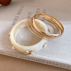 Detail of cream marbled resin bangle with starfish and gold textured bracelets