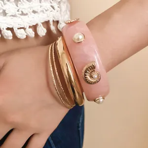 Close-up of pink resin bangle with shell and pearl details on a model's wrist