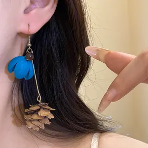 Detail shot of forest style drop earrings with blue flower and pinecone pendant on ear