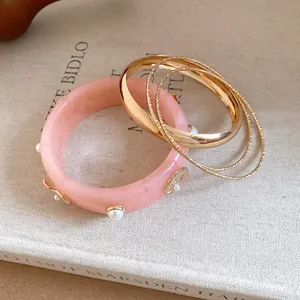 Close-up of pink resin bracelet with gold charms and matching metal bangles
