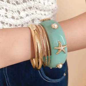 Close-up of bohemian mint resin starfish bangle and gold bracelets set for women