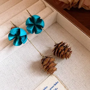 Detailed view of forest-inspired earrings with blue fabric flowers and pinecone pendants