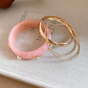 Detailed macro view of pink resin starfish bangle paired with textured gold bangles on a book