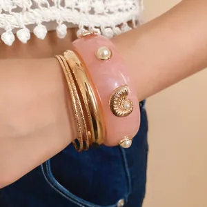 Close-up detail of pink resin shell bracelet with gold bangle set on female wrist