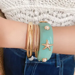 Close-up of Bohemian resin starfish bangle and gold metal bracelet stack set on wrist