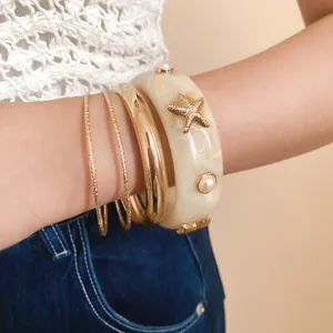 Detailed macro shot of chunky cream resin starfish bangle and layered gold metal bracelets