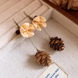 Close-up of vintage forest-style earrings with cream flowers and natural pinecone pendants.