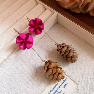 Close-up of vintage forest style earrings with magenta flowers and pinecone pendants