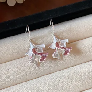 Dettaglio macro di orecchini a foglia increspata in smalto bianco e rosa.