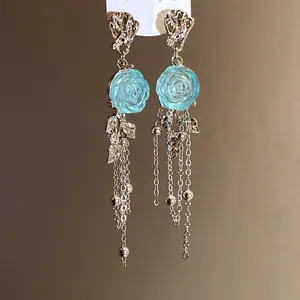 Macro detail of elegant silver tassel earrings featuring a blue resin rose design