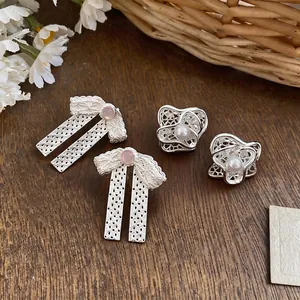 Squisiti orecchini a fiocco e fiori in argento con perle su fondo in legno naturale