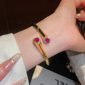Dettaglio del bracciale rigido aperto placcato oro 18k con zirconi rosa a goccia al polso.