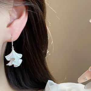 Dettaglio ravvicinato di un orecchino a foglia pieghettata in smalto bianco su orecchio.