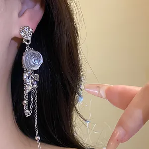 Close-up detail of elegant silver tassel earrings featuring a white resin rose blossom
