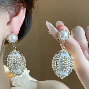 Close-up view of a vintage oval pearl drop earring with intricate white enamel details.