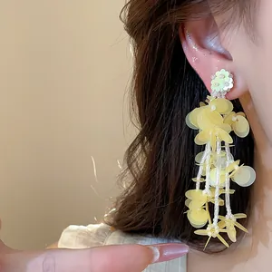Close-up of yellow floral tassel earrings with gold-plated finish on model's ear