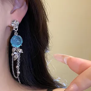 Detailed close-up view of elegant blue resin rose and silver tassel earring on a model's ear