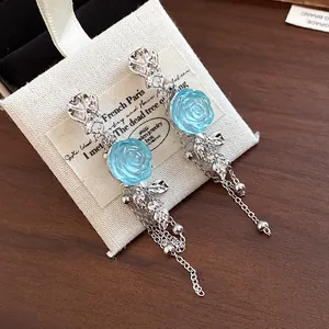 Close-up of silver tassel earrings with blue resin rose and metal leaf detail