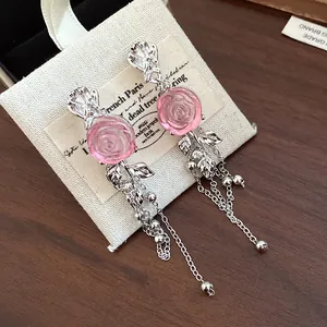 Close-up of pink resin rose tassel earrings on a linen jewelry pouch