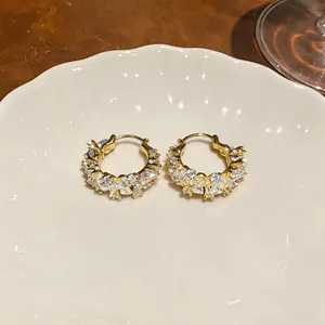Detail of 14k gold-plated hoop earrings with sparkling zircon on a ceramic plate.