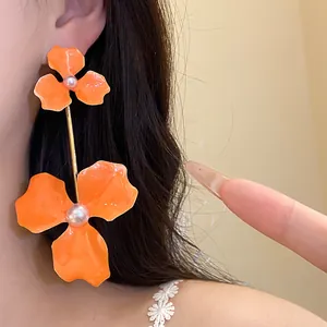 Detail der übergroßen orangefarbenen Emaille-Blumenohrringe mit Perlen am Ohr
