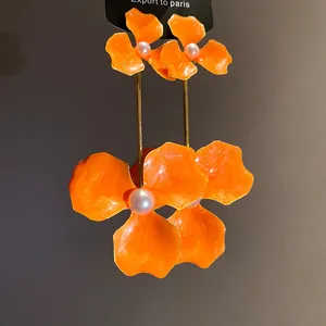 Makroansicht von leuchtend orangefarbenen Blumenohrringen mit eleganten Perlenmitten