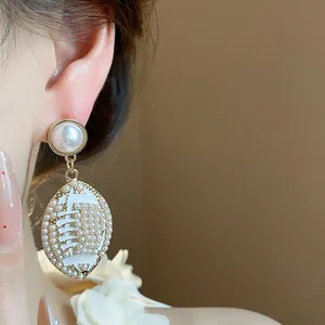 Elegant close-up detail of pearl-encrusted football-shaped drop earrings in gold