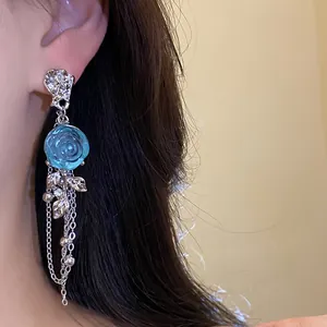 Close-up of elegant blue resin rose earrings with long silver tassels worn on ear