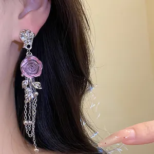 Close-up of elegant pink resin rose dangling earrings with silver chain tassels.