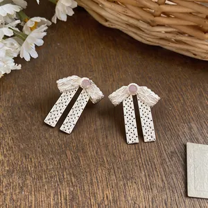 Primo piano di orecchini a fiocco in pizzo bianco con pietra rosa su fondo in legno