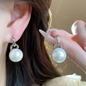 Primo piano di eleganti orecchini di perle con ago d'argento indossati e tenuti