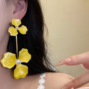 Detailaufnahme gelber Emaille-Blumenohrringe mit Perlenakzenten an einem Modell