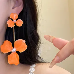 Nahaufnahme auffälliger orangefarbener Blumenohrringe mit Perlen und Goldstab.