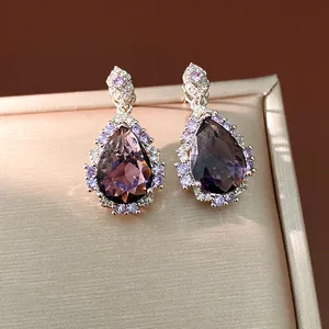 Close-up of elegant purple teardrop zircon earrings on a champagne jewelry box