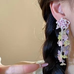 Close-up detail of multi-colored glass beaded flower drop earrings on an Asian model ear
