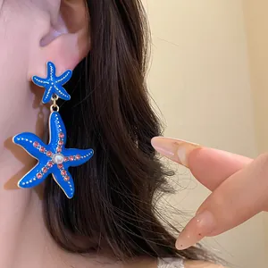 Dettaglio di orecchini a stella marina blu con perla e strass rosa indossati all'orecchio