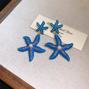 Dettaglio orecchini a stella marina in smalto blu con strass rosa e perla centrale.