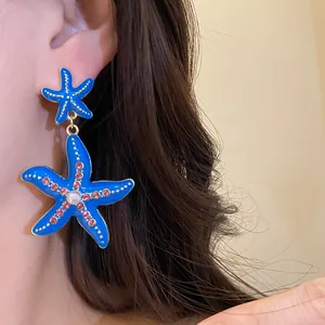 Dettaglio di orecchini a stella marina in smalto blu con strass rosa e una perla