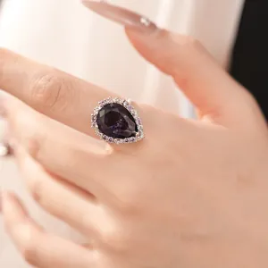 Close-up of elegant teardrop-shaped purple zircon ring with crystal halo on finger
