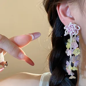 Detailed close-up view of handmade pastel glass flower beaded tassel earrings worn on ear