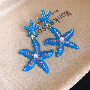 Dettaglio di orecchini a stella marina in smalto blu con strass e perla centrale.