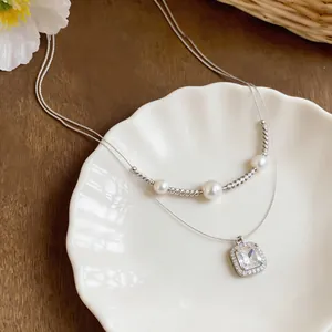 Primo piano della collana a strati con ciondolo in zircone quadrato e perle su piatto bianco.