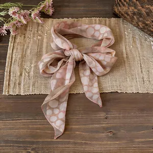 Sciarpa a nastro in chiffon con stampa a pois rosa legata a fiocco su tappeto in legno