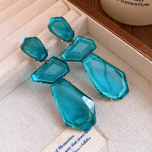 Vista dettagliata di grandi orecchini pendenti in resina blu con montatura in metallo dorato.