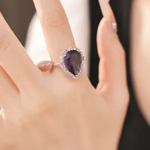 Detail of a pear cut purple zircon ring in a luxury palace style setting on a finger.