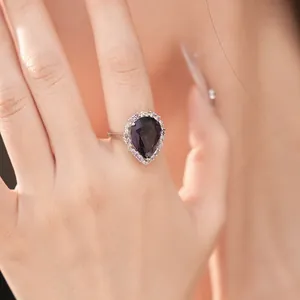 Close-up detail of a silver-tone palace style ring with pear-cut purple zircon on hand.